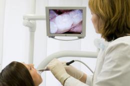 Eine Patientin wird mit der intraoralen Kamera untersucht und betrachtet ihre Befunde dabei auf dem Bildschirm